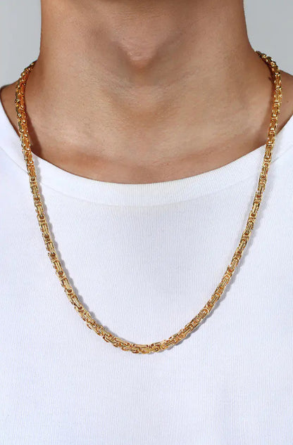 Gold necklace worn by a person on a plain background 