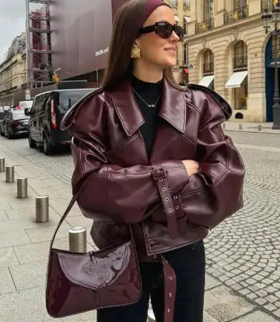 Woman wearing a burgundy leather jacket and matching handbag on a city street.